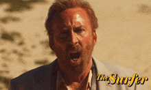 a man with a beard is screaming in front of an ad for the surfer