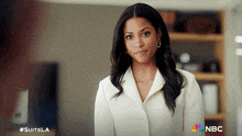 a woman in a white coat is standing in front of a nbc logo