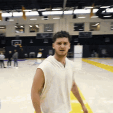 a man in a white tank top stands in a gym