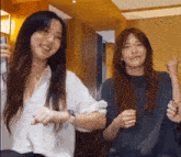two women are standing next to each other in a room and smiling . one of the women is wearing an apple watch .