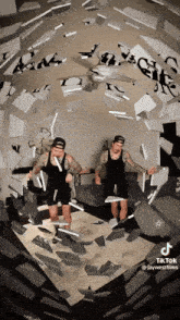 two men are standing in a room with a ceiling fan and a clock behind them