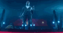 a man in a tuxedo is standing on a balcony holding a microphone in a dark room .