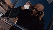 a bald man is standing in front of a car looking out the window .