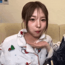 a woman wearing a pajama top with a christmas tree on it looks at the camera
