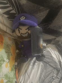 a stuffed mario is laying on a bed next to a phone