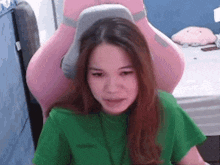 a woman in a green shirt is sitting in a pink chair and making a funny face .