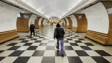 a man in a black jacket walks through a checkered hallway