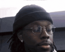 a man wearing glasses and a beanie is looking at the camera