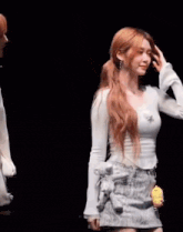a woman in a white shirt and a denim skirt is holding a teddy bear .