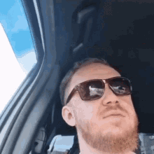 a man with a beard is sitting in a car wearing sunglasses .