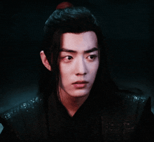 a young man with long hair and a ponytail looks at the camera with a serious look on his face .