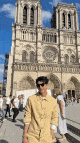 a man wearing sunglasses stands in front of a large cathedral