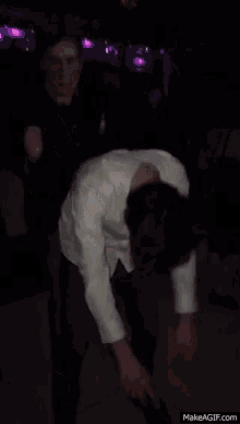 a man in a white shirt is dancing with his arms outstretched in a dark room .