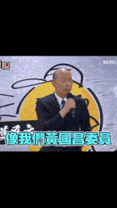 a man in a suit and tie is speaking into a microphone with chinese writing on the screen