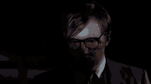 a man wearing glasses and a suit is looking up at something in the dark