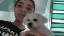 a woman in a black shirt is holding a small white dog in her arms .