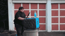 a man is holding a sword and a bottle of water in front of a garage .