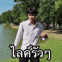 a man in a white shirt is standing in front of a body of water with trees in the background