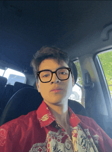 a young man wearing glasses and a red shirt is in a car