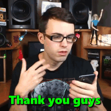 a man wearing glasses holds a cell phone and says thank you guys in green letters