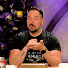 a man wearing a ulnera jagrant t-shirt sits with his eyes closed