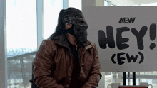 a man wearing a mask sitting in front of a sign that says hey
