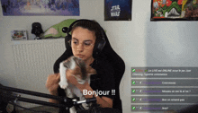 a woman holding a kitten in front of a microphone with a star wars poster on the wall behind her
