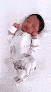 a baby wearing a white outfit with rainbows on it is laying on a bed