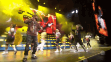 a group of people are dancing on a stage with a large screen behind them that says i love you