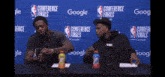 two men sitting at a table in front of a conference finals sign