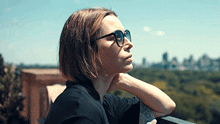 a woman wearing sunglasses and a black shirt looks out over a city