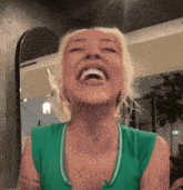 a woman wearing a green tank top is laughing with her mouth open