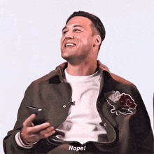 a man is holding a cell phone and smiling while wearing a jacket with flowers on it .