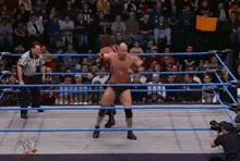 two men are wrestling in a wrestling ring while a referee stands behind them .