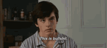 a young man in a striped shirt is standing in front of a door and says `` this is bullshit '' .