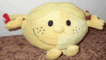 a yellow stuffed animal with a smiley face and freckles is sitting on a brown surface .