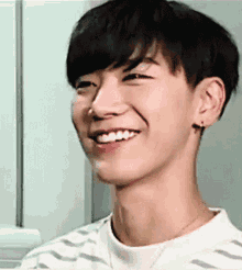 a young man is smiling and wearing a striped shirt and earrings .
