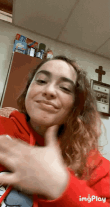 a woman in a red hoodie is giving a thumbs up in front of a cross