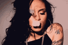 a woman is smoking a cigarette and blowing smoke out of her mouth .