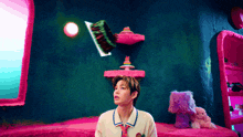 a man in a white shirt and tie is standing in a pink room with a cake on a shelf on his head .