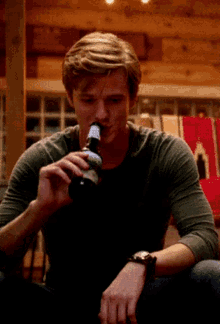 a man in a green shirt is drinking from a bottle with a label that says ' beer ' on it