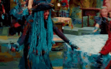 a woman with blue hair and a pirate hat is standing next to a table in a room .