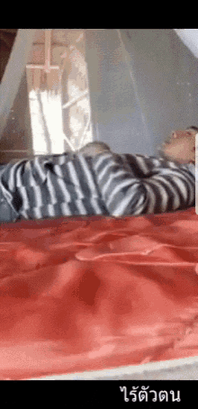 a man in a striped shirt is laying on a bed with red sheets