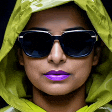 a woman wearing sunglasses and purple lipstick is wearing a green hooded jacket