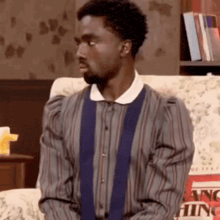 a man in a striped shirt and tie is sitting on a couch with a pillow that says nothing