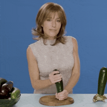 a woman holds a cucumber on a cutting board