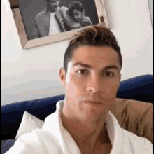 a man in a white robe is sitting on a couch in front of a framed picture of a man and a child .