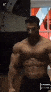 a man without a shirt is standing in a gym with his arms outstretched .