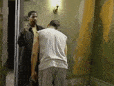 a man in a white tank top is standing next to another man in a black jacket