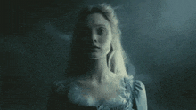 a woman in a blue dress is standing in a dark room looking at the camera .